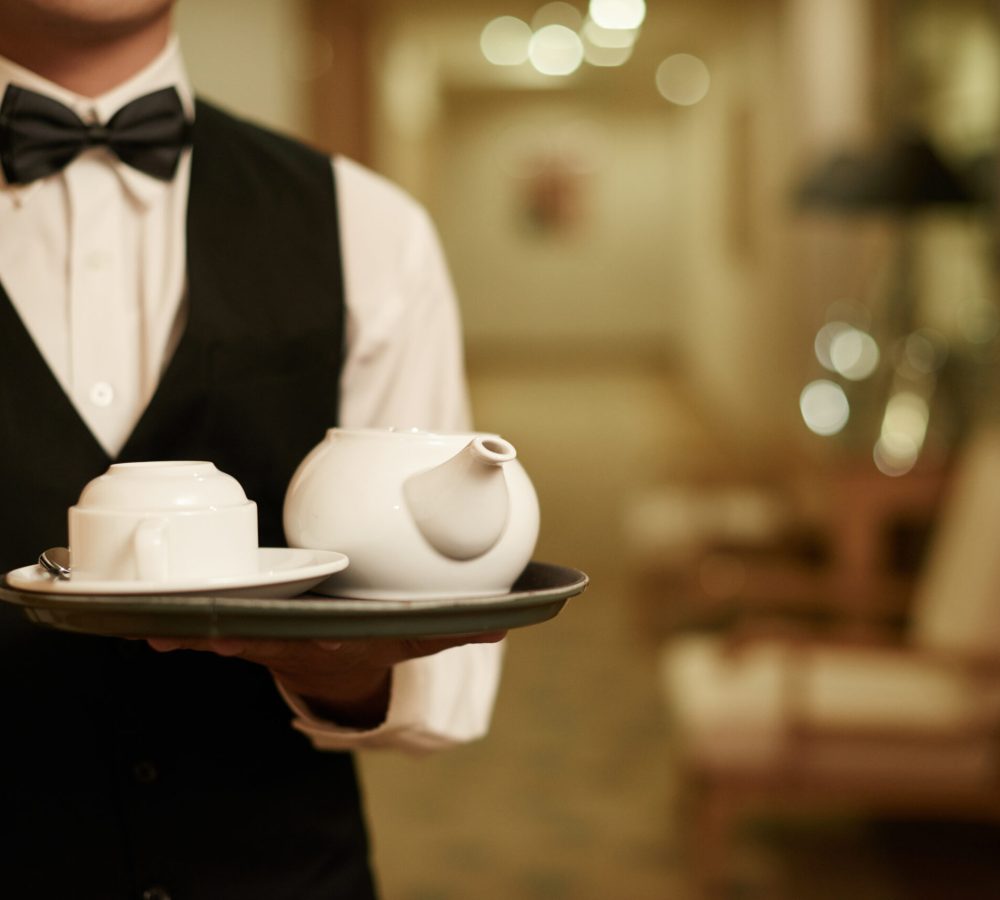 Cropped image of waiter holding tray with teapot and cup